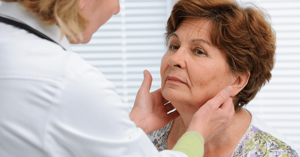A doctor checking the thyroid glands of an old-aged woman with swollen face